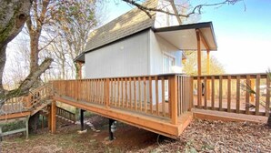 Un molo in legno conduce a un edificio bianco con tetto spiovente, circondato da alberi.