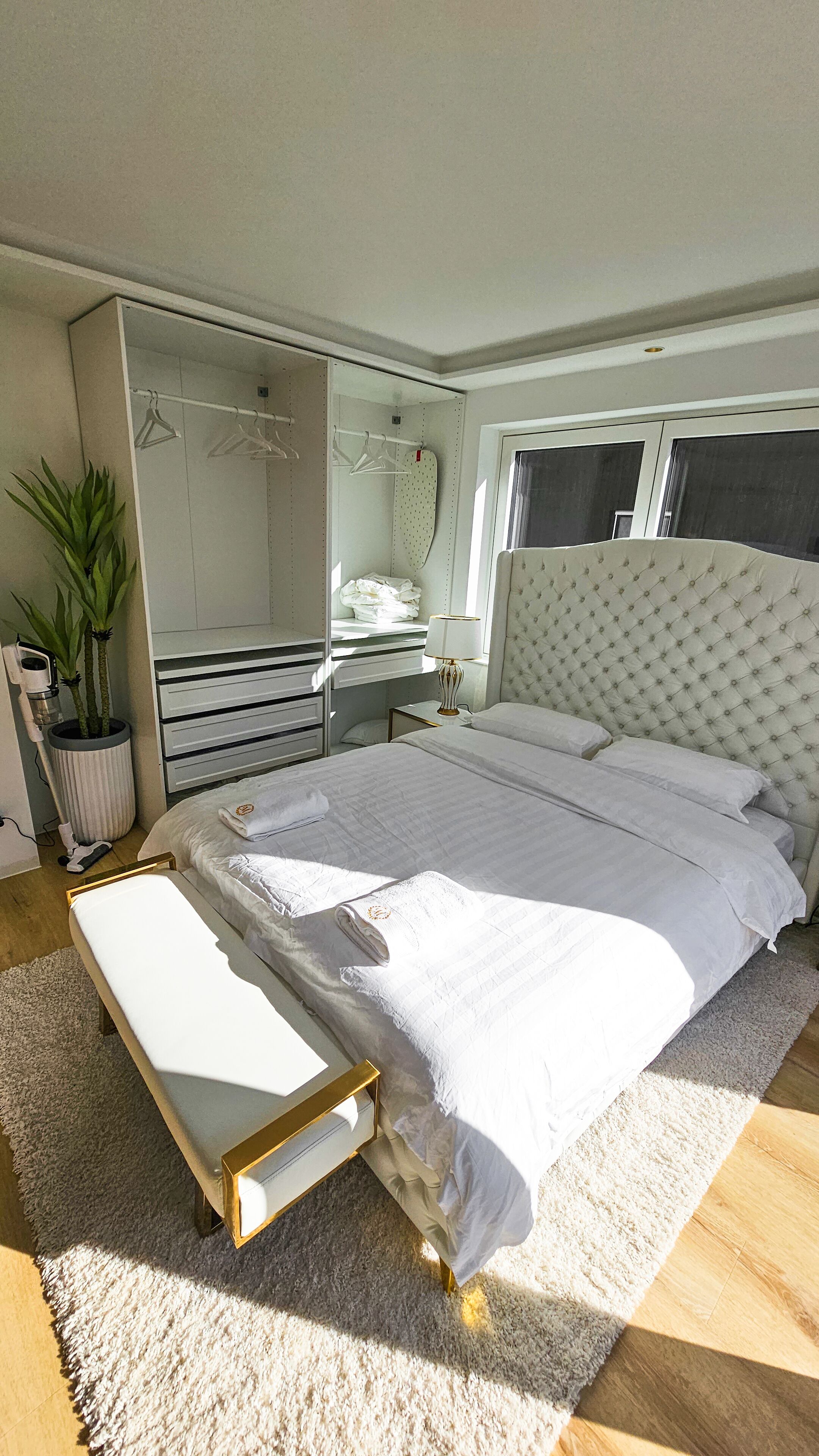 A bedroom with a bed, bedside table, lamp, dresser, mirror, and potted plant.