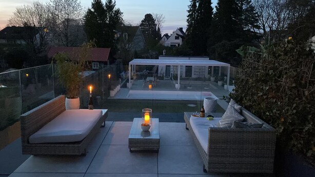 Eine Außenpatio mit Sitzgelegenheiten, einer Glasbrüstung und Blick auf ein Haus und Bäume.