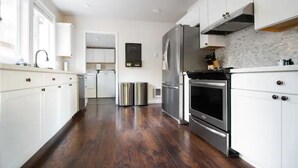 A modern kitchen with white cabinets, stainless steel appliances, and a wooden floor.