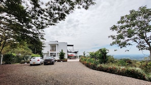 Un edificio moderno de dos plantas con camino de grava y coches aparcados.