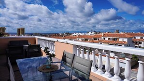 Une terrasse sur le toit, avec une table et des chaises, une vue sur le paysage urbain et une balustrade blanche.