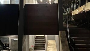 Een moderne entree van een gebouw met een glazen deur, een trap en een geparkeerde auto.