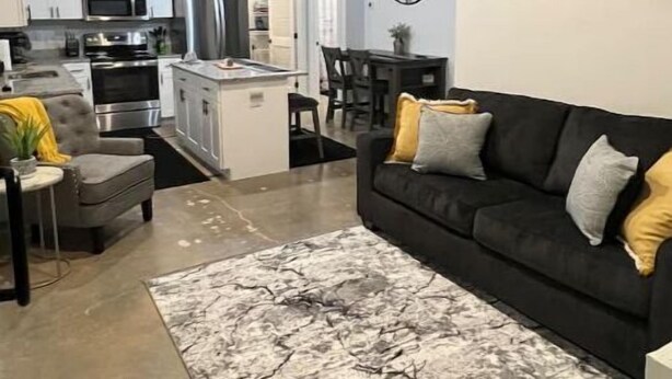 Een moderne woonkamer met een zwarte bank, een vloerkleed met een marmerprint en een eethoek met een kroonluchter.
