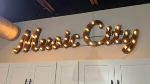 Een bord met verlichte letters waarop 'Music City' staat, bevestigd aan een muur.