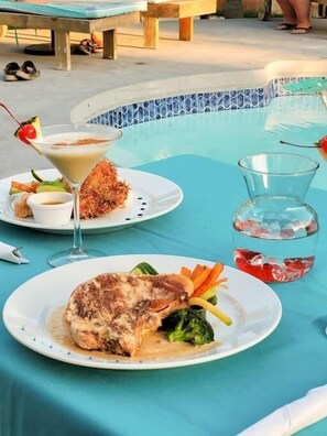 A dining table with a meal consisting of a steak, vegetables, and a martini.
