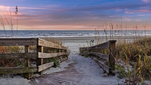A wooden boardwalk leading to a beach with a view of the ocean and sky.