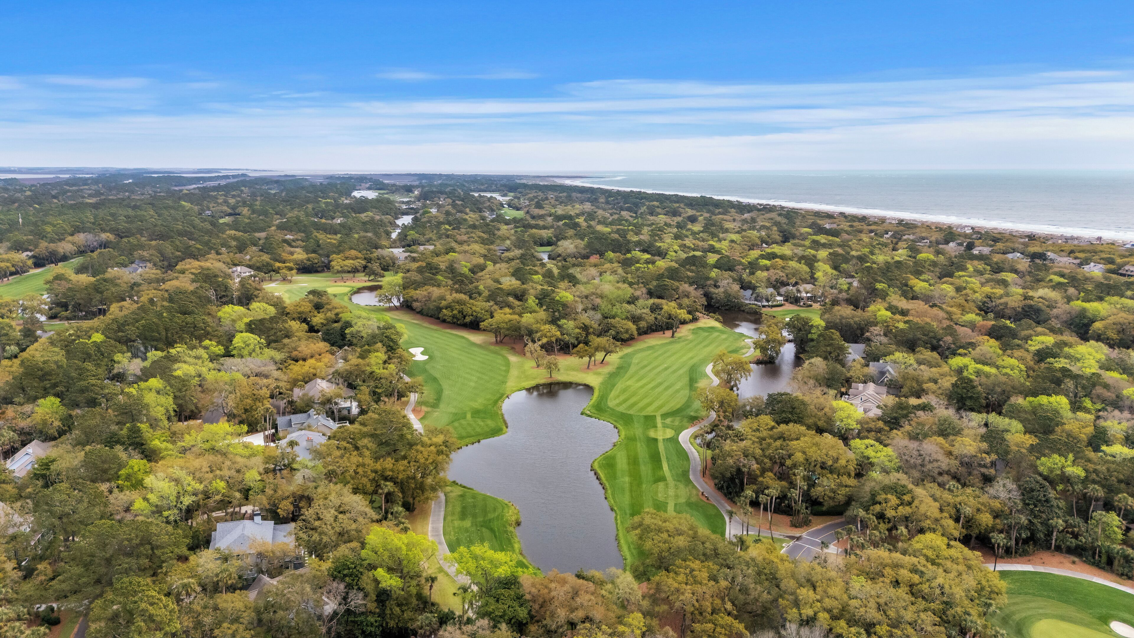 Ein Golfplatz mit Teich, umgeben von dichter Vegetation und Blick auf den Ozean.
