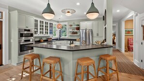 A kitchen with a central island, bar stools, stainless steel appliances, and pendant lighting. - Stunning 7 BR Home on Eugenia, Private Pool, 100 yards to Beach! (Kiawah Island)