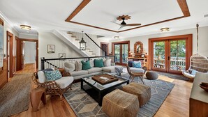 A spacious living room with a staircase, wicker furniture, and a large window with a view. - Stunning 7 BR Home on Eugenia, Private Pool, 100 yards to Beach! (Kiawah Island)