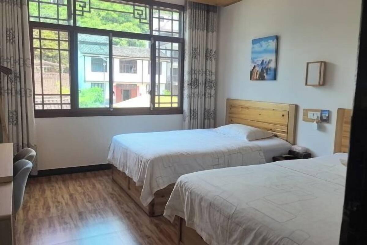 Een kamer met twee bedden, een houten vloer, een raam met uitzicht op gebouwen en een schilderij aan de muur.