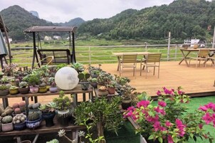 A terrace with potted plants, a swing, and a view of a green landscape.