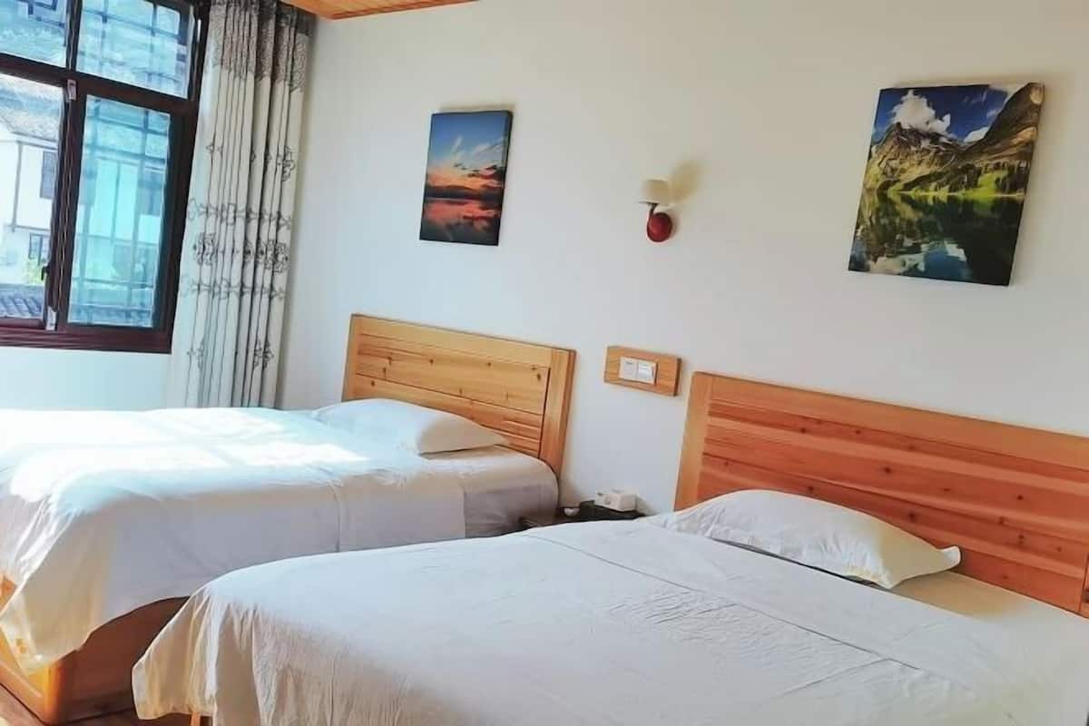 Een hotelkamer met twee bedden, een raam met gordijnen en twee aan de muur bevestigde schilderijen.