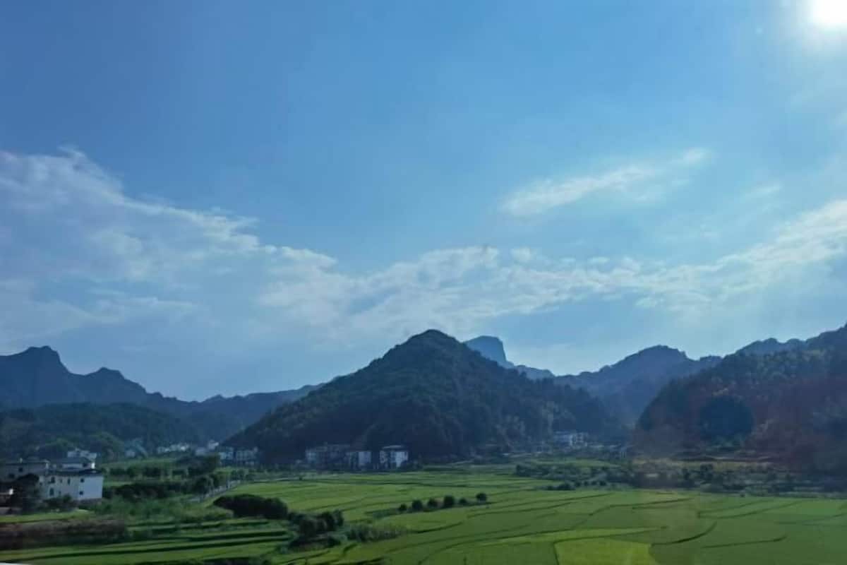 Een landelijk landschap met groene velden, een berg en een wit gebouw.