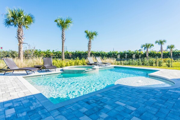 Relax by the clear pool surrounded by a paved deck and lounge chairs.