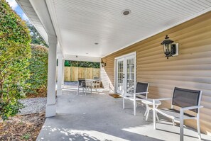 A covered patio with white chairs and a table, wooden siding walls, and a wooden fence in the background.
