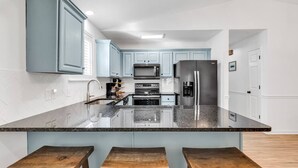 Une cuisine moderne avec des meubles de couleur bleu clair, un plan de travail en granit, des appareils électroménagers en acier inoxydable et des tabourets en bois.