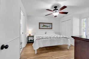 A bedroom with a bed, a ceiling fan, a framed picture, and a window with blinds.