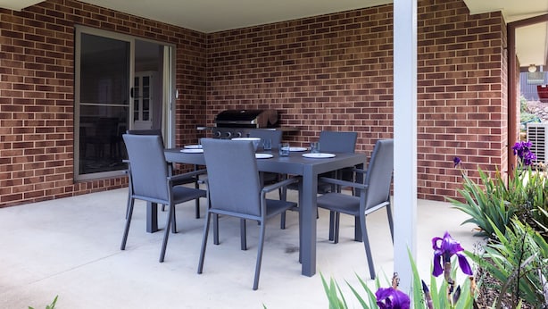 Eine Terrasse im Freien mit Backsteinmauer, einer Glasschiebetür, einem Grill und einem Tisch für vier Personen.