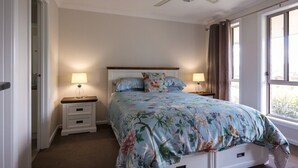 Ein Schlafzimmer mit einem Bett, zwei Nachttischen mit Lampen, einem Deckenventilator und einem Fenster mit Vorhängen.