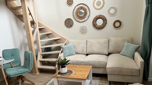 A living room with a wooden staircase, a beige sofa, a teal armchair, a wooden coffee table, and a patterned rug. - Casa Kashubia Sansibar - Premium vacation home by the lake - near the Baltic Sea (Brzezno Szlacheckie)