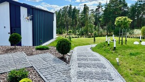 A modern building with a paved pathway leading to it, surrounded by a well-maintained garden and a forested area. - Casa Kashubia Sansibar - Premium vacation home by the lake - near the Baltic Sea (Brzezno Szlacheckie)