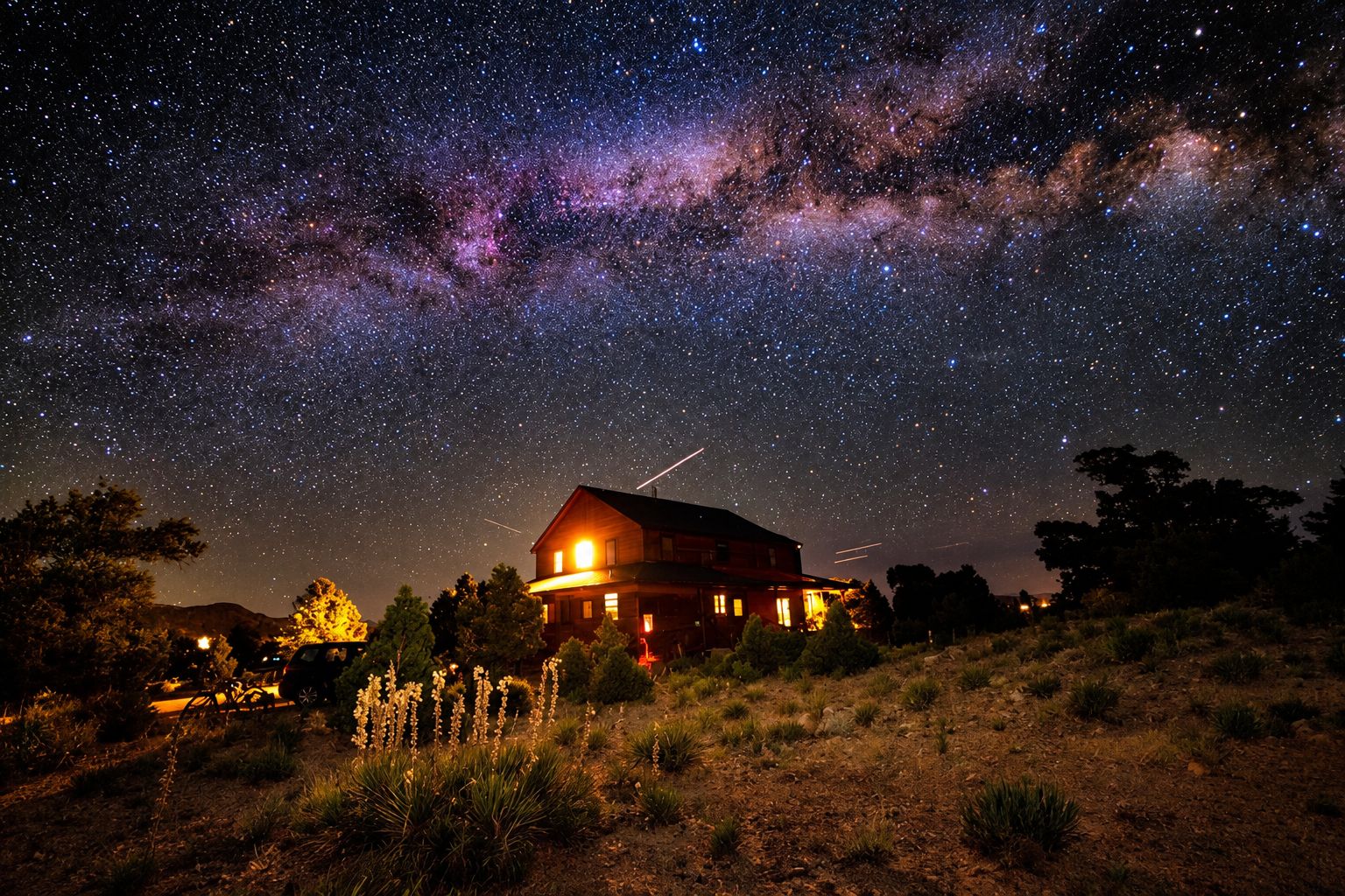 A house with a starry night sky view, surrounded by dry grass and trees.
