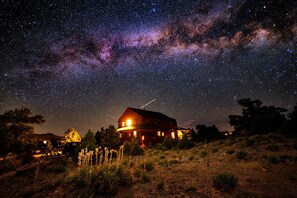 Una casa con vista a un cielo estrellado, rodeada de hierba seca y árboles.