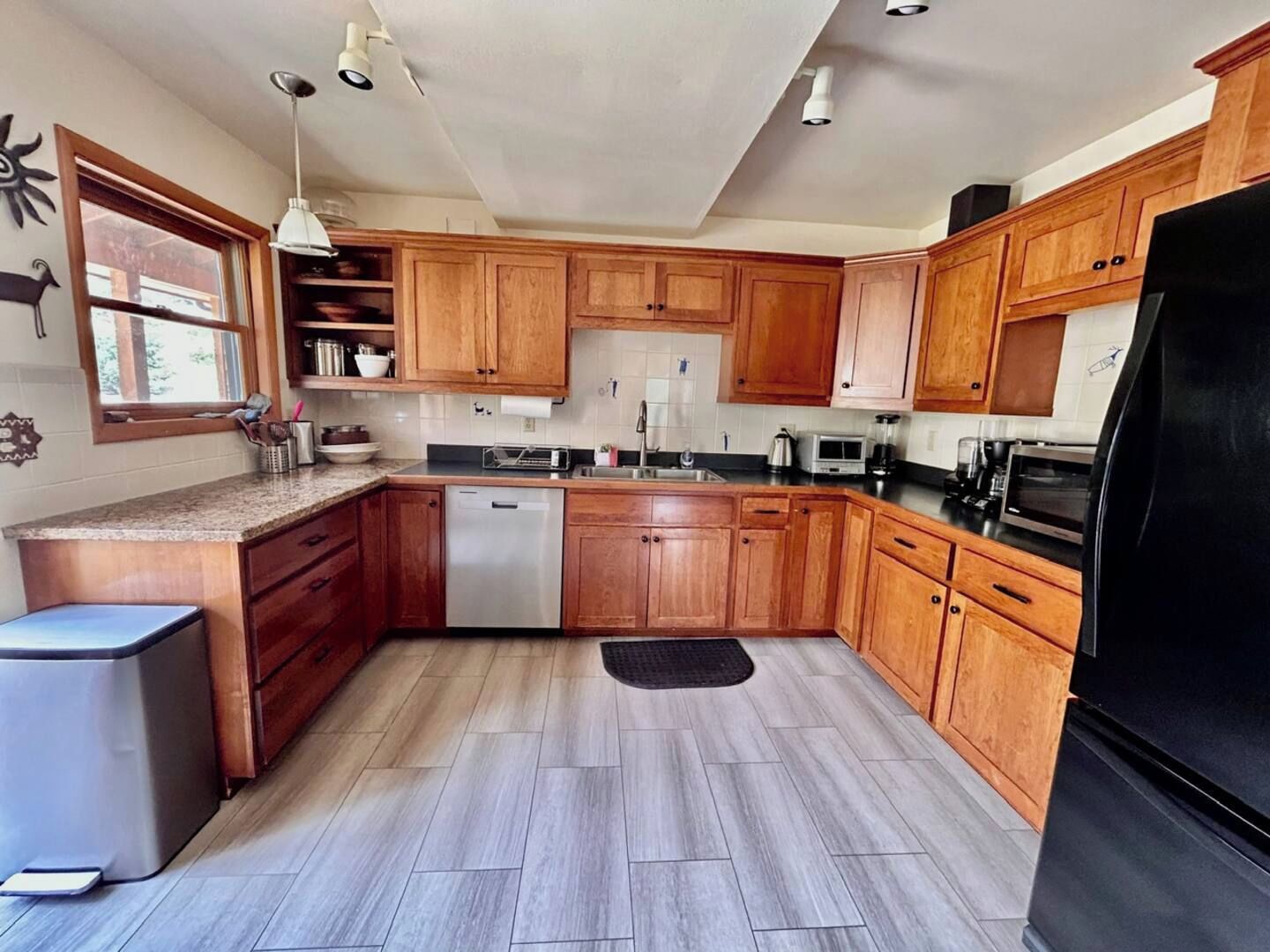 A kitchen with wooden cabinets, a dishwasher, a refrigerator, and a window.
