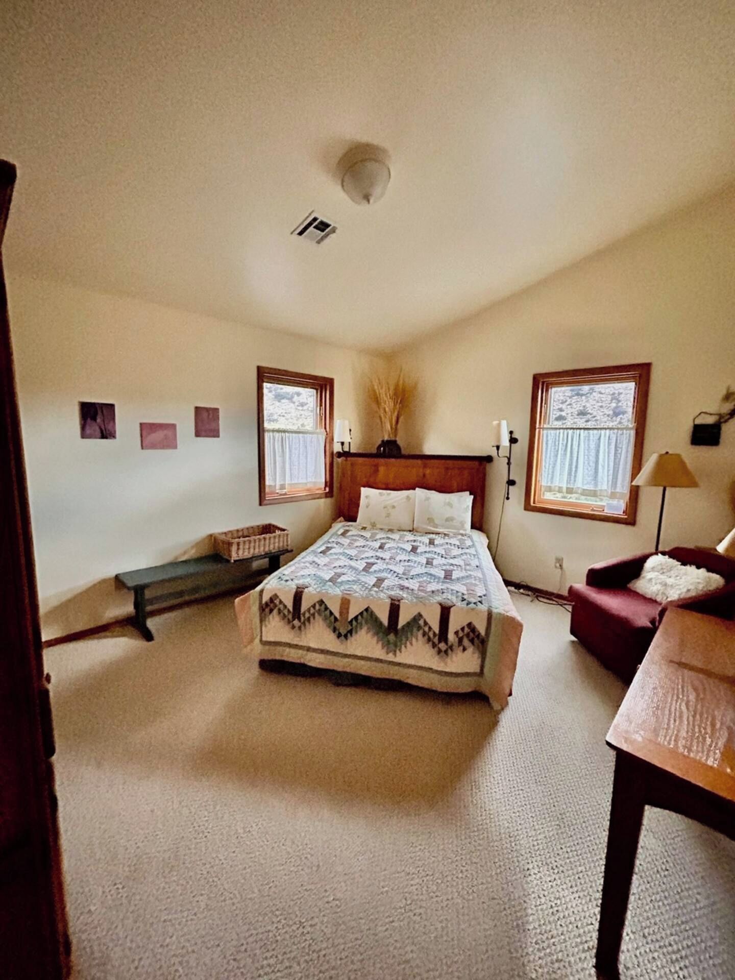 A bedroom with a bed, two windows, a bedside table, a chair, and a lamp.