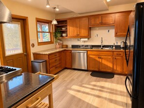 Una cocina con armarios de madera, lavavajillas de acero inoxidable, refrigerador negro y una ventana con persianas.