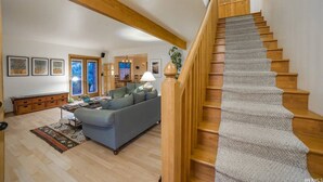 Un salon spacieux avec un canapé gris, un escalier en bois et un coin repas visible à travers une porte ouverte.