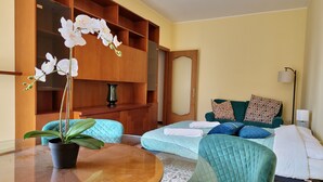 A hotel room with a round wooden table, a potted plant, a sofa with a quilted green cover, and a bed with a white duvet and blue pillows. - Garden on the Naviglio (Milano)