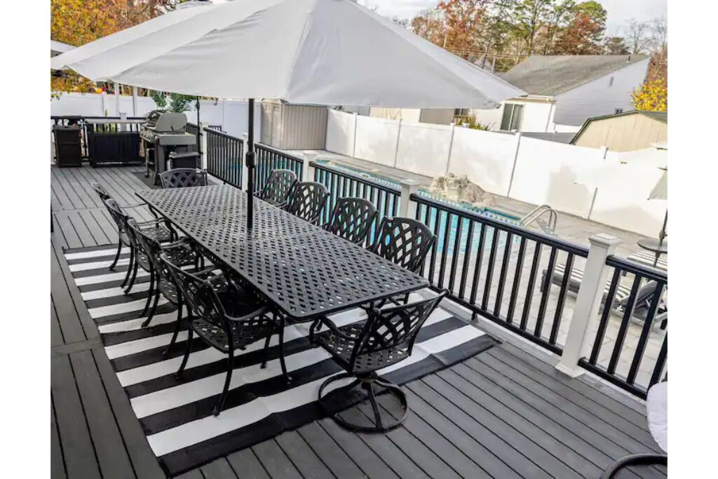 A covered outdoor patio with a long table and chairs, surrounded by a black metal railing.