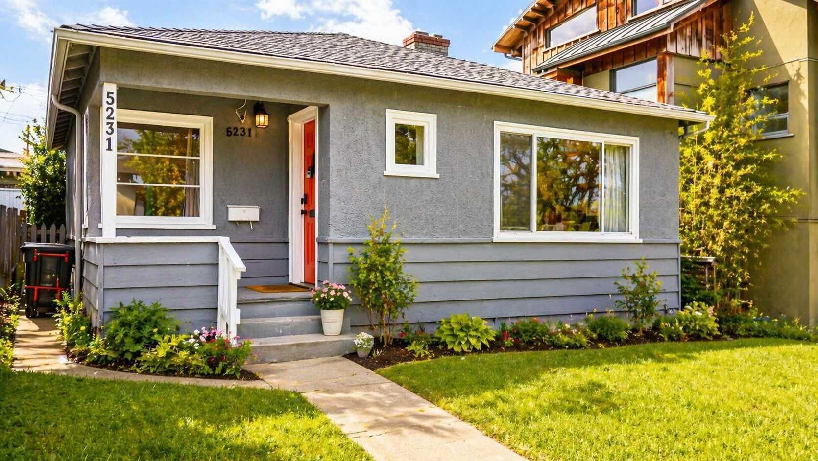 A single-story house with a grey exterior, white trim, a red door, and a small front porch with steps.