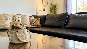 Uma sala de estar com sofá de couro preto, mesa de centro de madeira e um cesto de vime com plantas.
