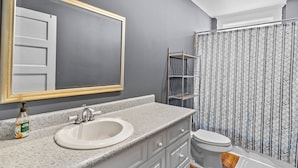 A bathroom with a granite countertop sink, a large mirror, a toilet, and a shower curtain with a chevron pattern.