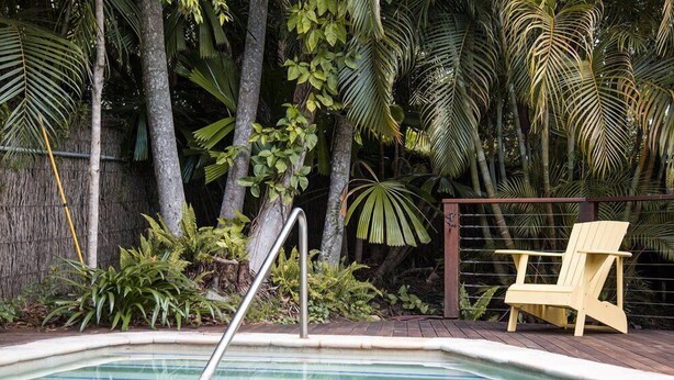 Una piscina con cubierta de madera, rodeada de plantas tropicales y una silla amarilla.
