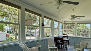A covered porch with wicker chairs, a dining table, and a ceiling fan. - Osprey Nest- Historic Cedar Key. Pet Friendly! (Cedar Key)