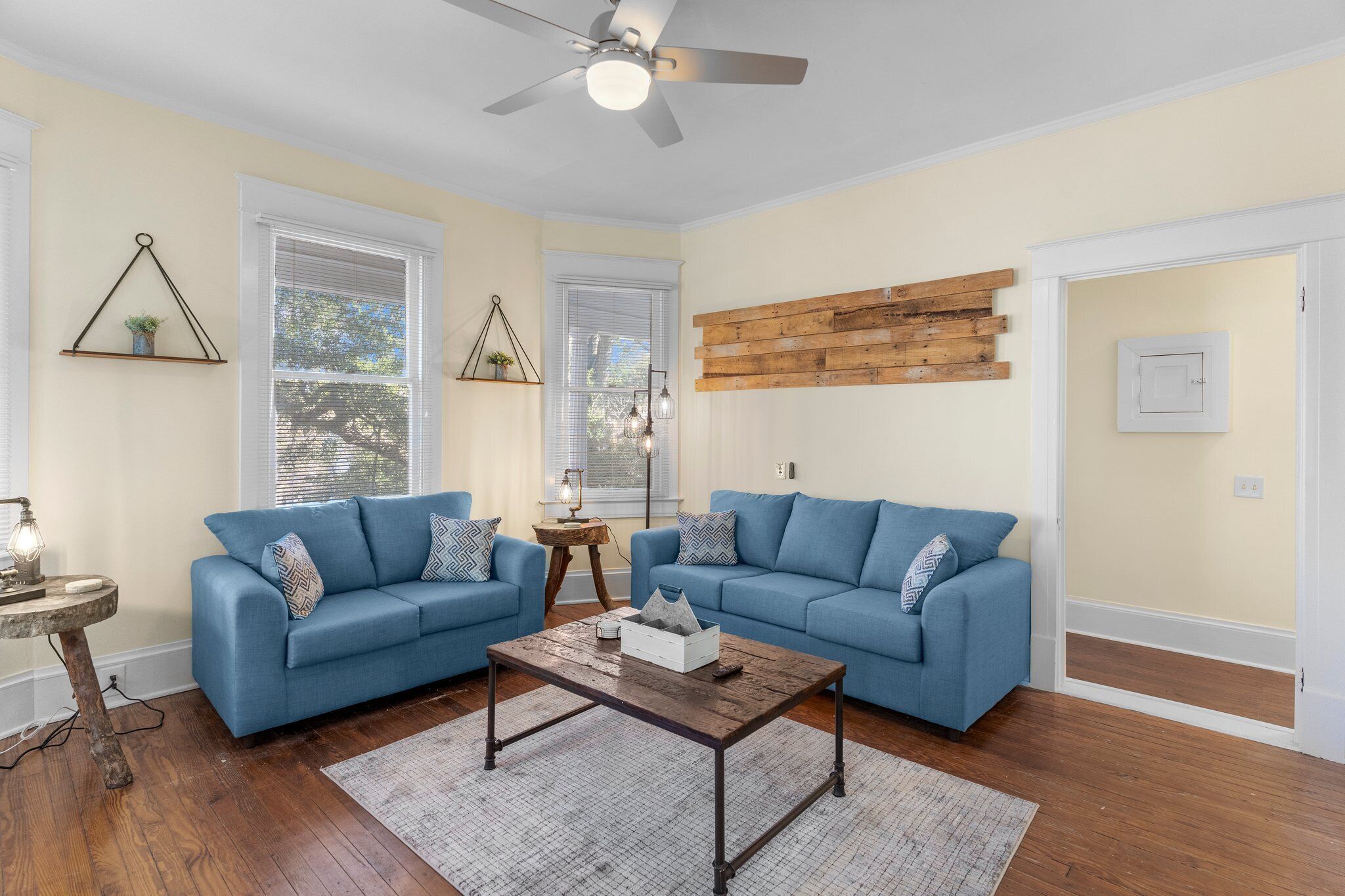 Un salon avec deux canapés bleus, une table basse en bois et un ventilateur de plafond.