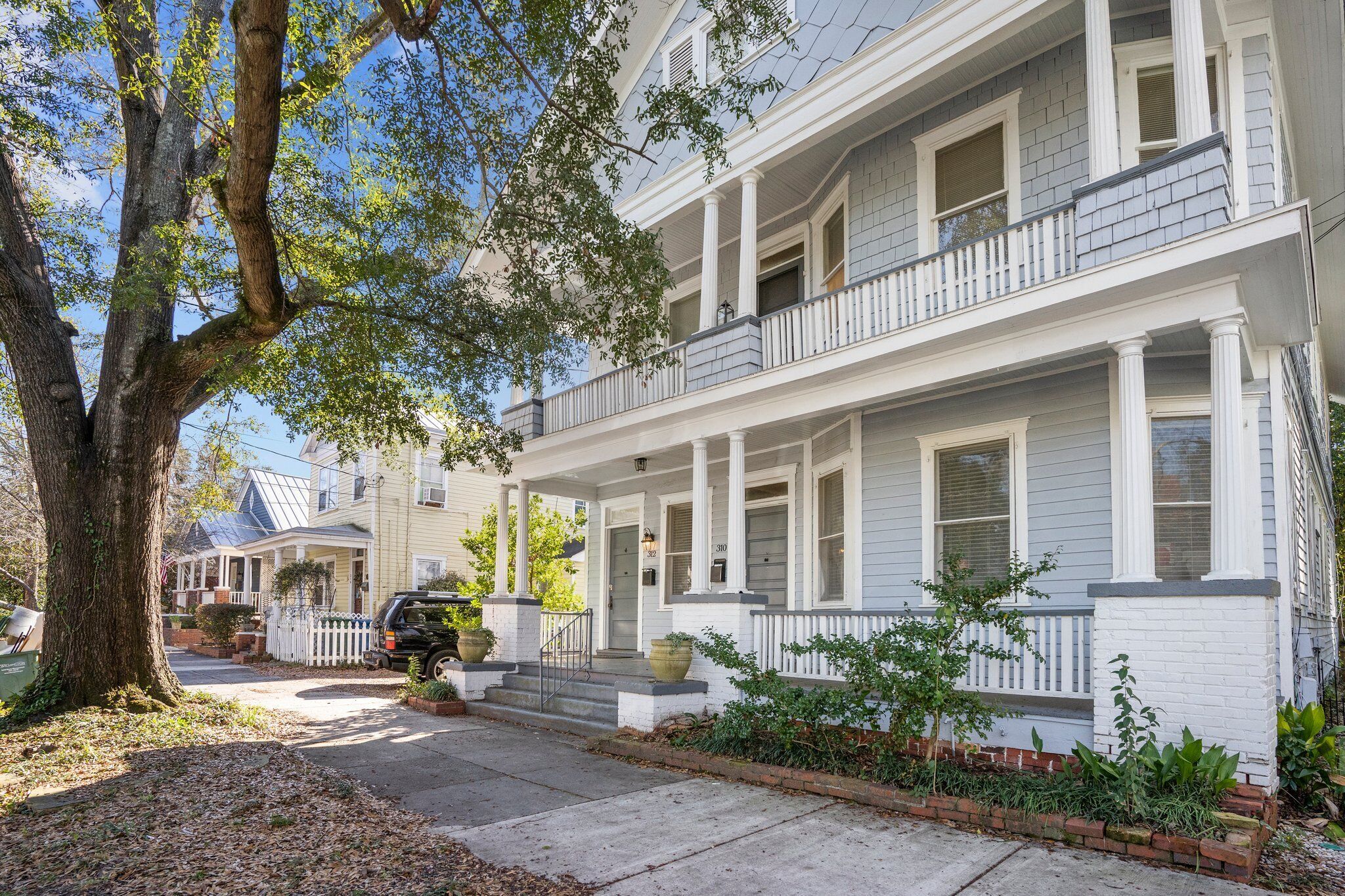 A two-story house with a front porch, a large tree, and a parked car.