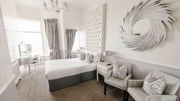 A modern bedroom with a large bed, a vanity, a chair, and a decorative mirror.