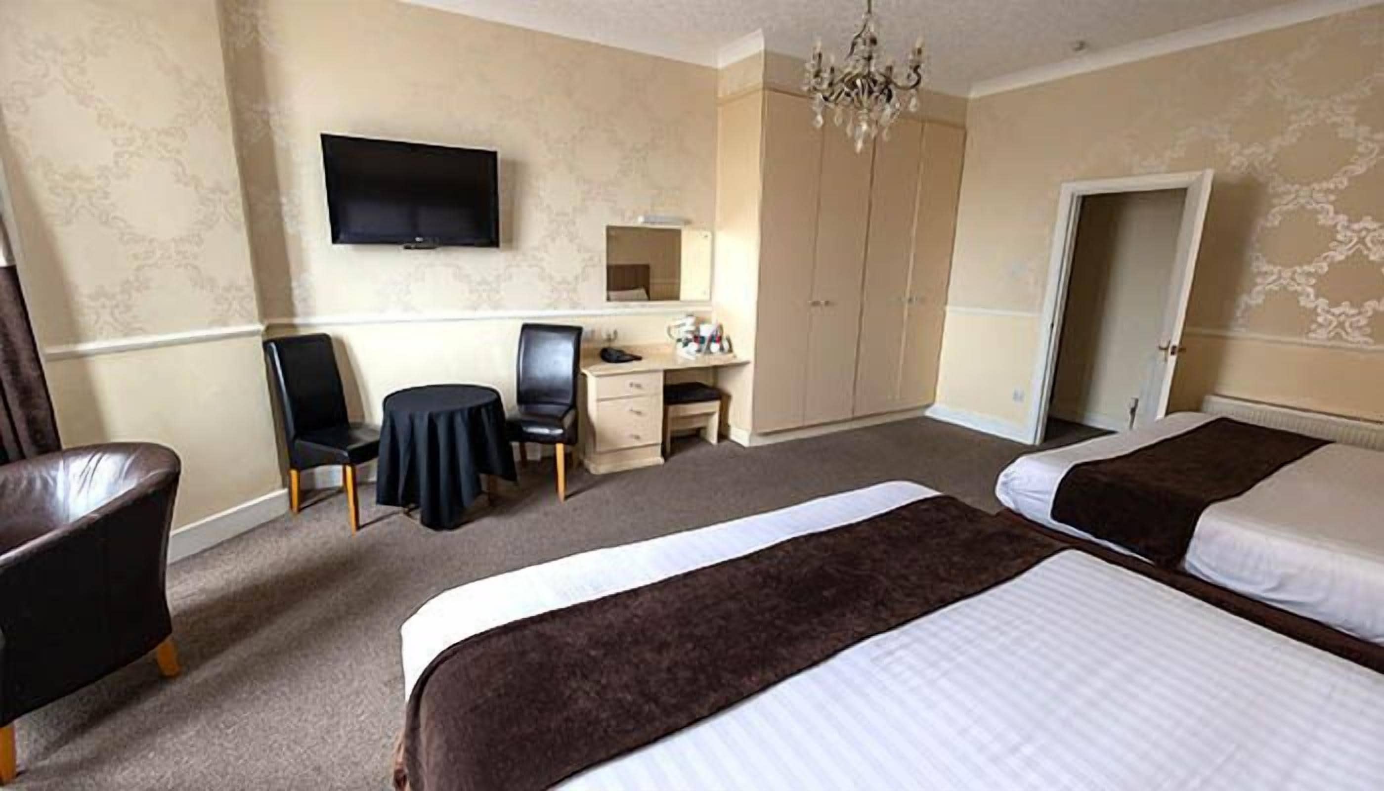 A hotel room with two beds, a desk with a chair, a television, and a wardrobe.