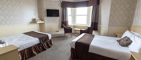 A hotel room with two single beds, a desk, a chair, a TV, and a window with curtains.