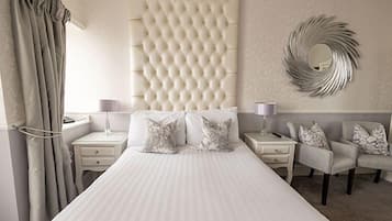 Een hotelkamer met een groot bed, twee nachtkastjes met lampen, een stoel en een decoratieve spiegel aan de muur.