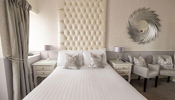 Een hotelkamer met een groot bed, twee nachtkastjes met lampen, een stoel en een decoratieve spiegel aan de muur.