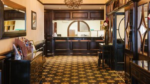 A lobby with a patterned carpet, a reception desk, and a chandelier.