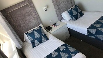 Een hotelkamer met twee bedden, elk met een blauw-witte bedspreide en passend kussen. Er staat een nachtkastje met een telefoon en een boek.
