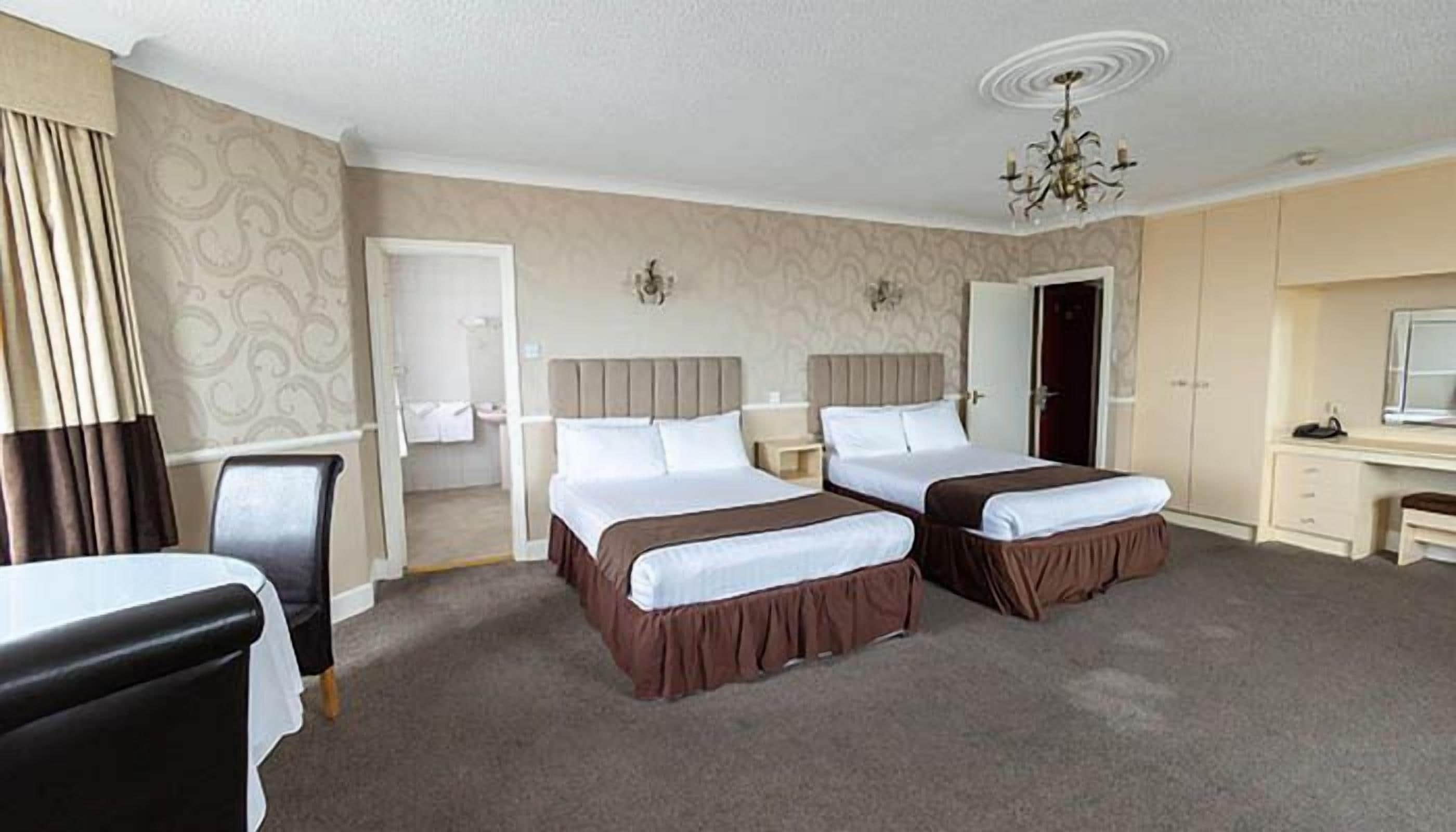A hotel room with two beds, a desk, a chair, a vanity, and a chandelier.