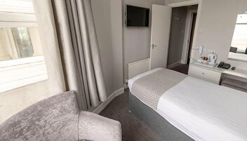 Een hotelkamer met een bed, een stoel, een bureau met telefoon en waterkoker, en een televisie aan de muur.
